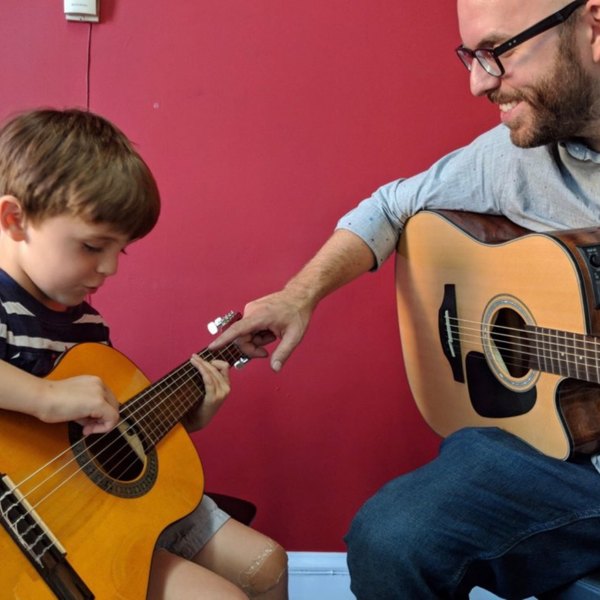 A teacher showing a young student where to put his fingers on an acoustic guitar